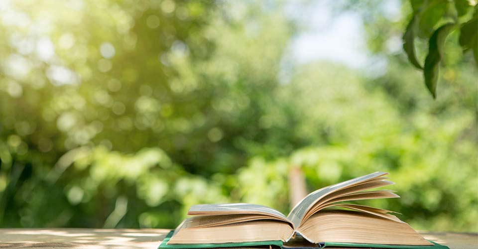 image of of open book on table in summer garden.